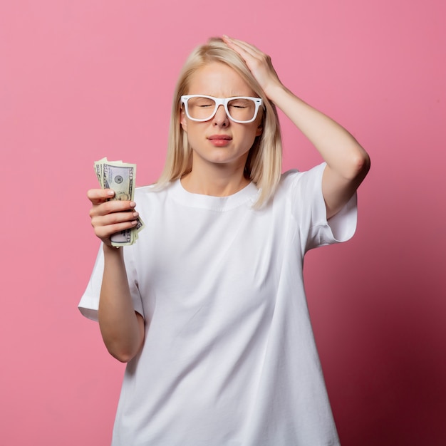 Blonde woman in white tshirt and glasses with money on pink