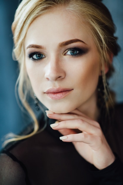 Blonde woman with blue eyes in a black dress in a dark turquoise interior