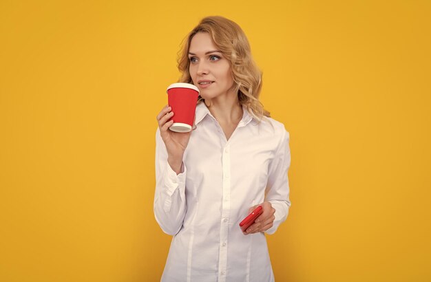 Blonde woman with coffee cup and smartphone on yellow background