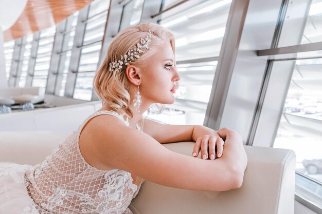 blonde woman with a creative hairstyle for short hair is sitting on a white sofa in t