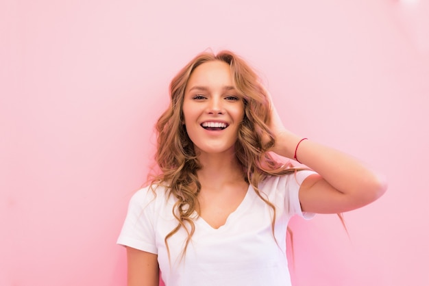 Blonde woman with curly beautiful hair smiling isolated on pink wall.