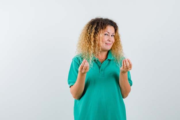 Blonde woman with curly hair doing Italian gesture in green T-shirt and looking sensible , front view.