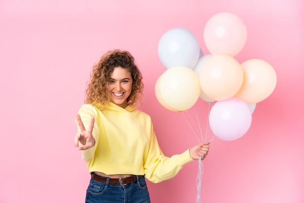 Blonde woman with curly hair holding many balloons