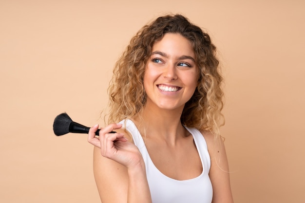 blonde woman with curly hair isolated holding makeup brush and looking up