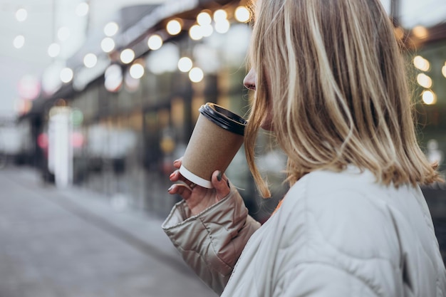 blonde woman with paper cup of drink on blurred bokeh background copy space