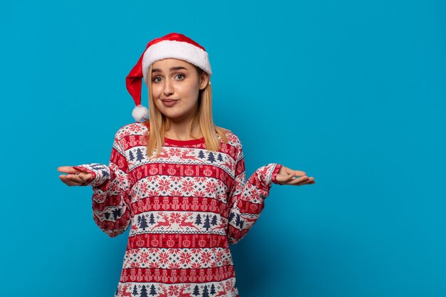 Blonde woman with santa hat feeling puzzled and confused, doubting, weighting or choosing different options with funny expression