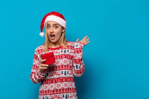 Blonde woman with santa hat screaming with hands up in the air, feeling furious, frustrated, stressed and upset