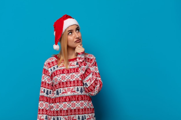 Blonde woman with santa hat thinking, feeling doubtful and confused, with different options, wondering which decision to make