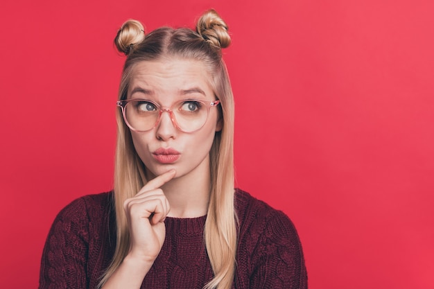 blonde woman with top-knots and glasses posing against the red wall