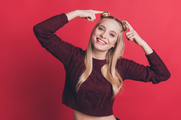 blonde woman with top-knots posing against the red wall