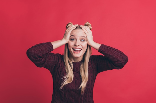 blonde woman with top-knots posing against the red wall