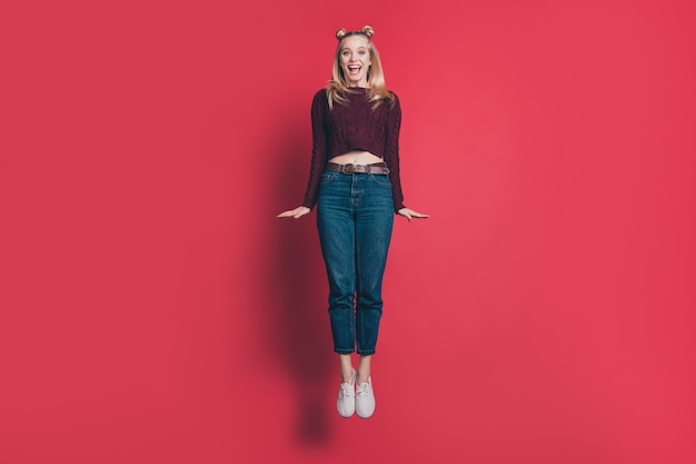 blonde woman with top-knots posing and jumping against the red wall