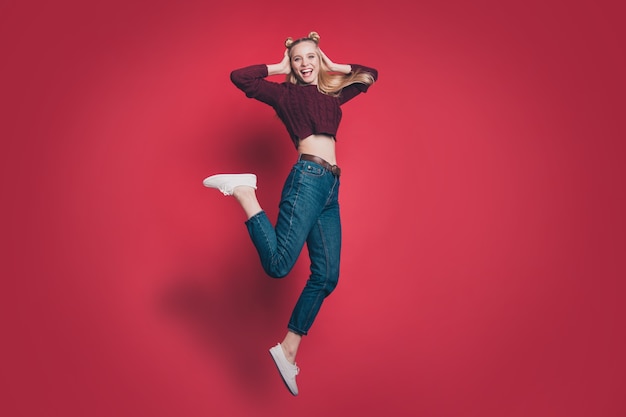 blonde woman with top-knots posing and jumping against the red wall