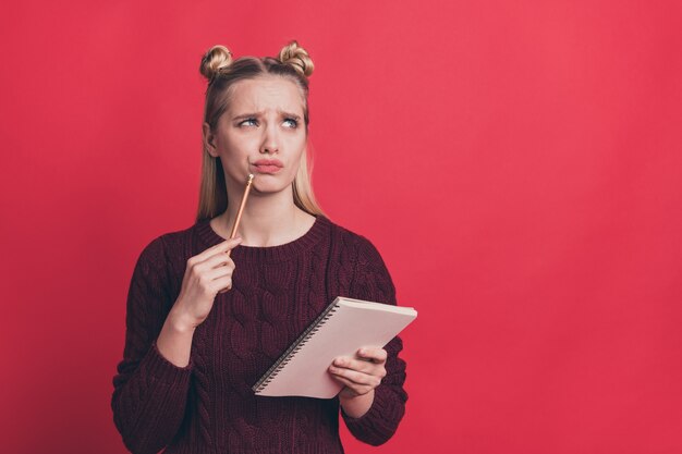 blonde woman with top-knots posing with a notebook against the red wall