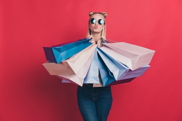 赤い壁に買い物袋でポーズをとってトップノットを持つブロンドの女性