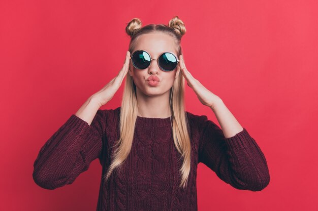 blonde woman with top-knots posing with sunglasses against the red wall