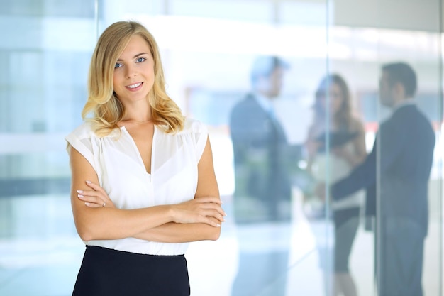 blonde woman with touchpad computer looking at camera and smiling while business people shaking hands over background
