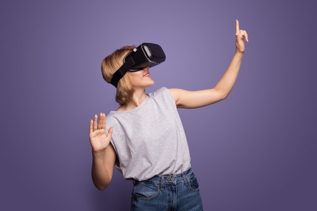 Blonde woman with vr headset is touching something while posing on a violet wall