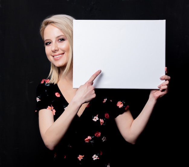 Blonde woman with white board on dark wall