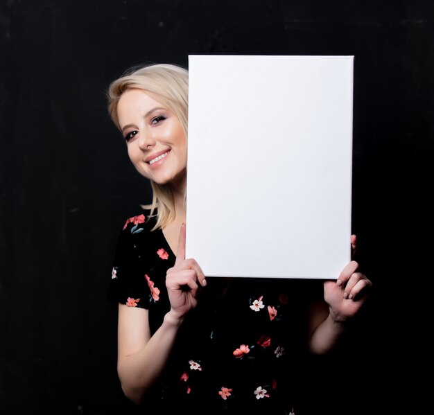 Blonde woman with white board on dark wall