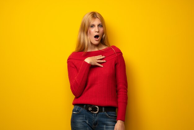 Blonde woman over yellow wall surprised and shocked while looking right