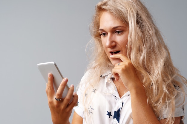 Blonde young casual woman looking at her phone over gray 