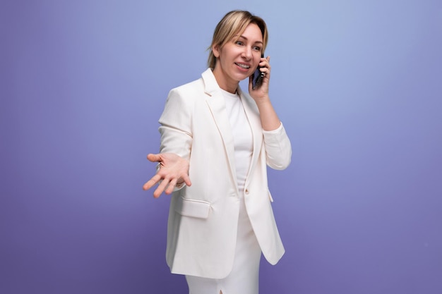 blonde young european woman dressed in a white jacket and dress talking on the phone