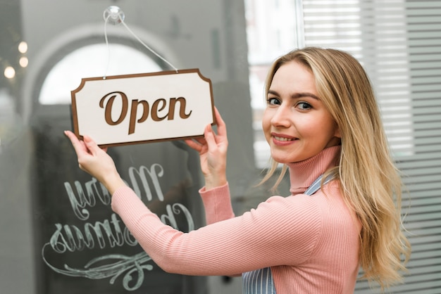 Photo blonde young woman hanging an open tag on the door entrance