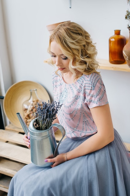 Blonde young woman holding flowers in a planting balcony interior. Healthy lifestyle, beauty, eco