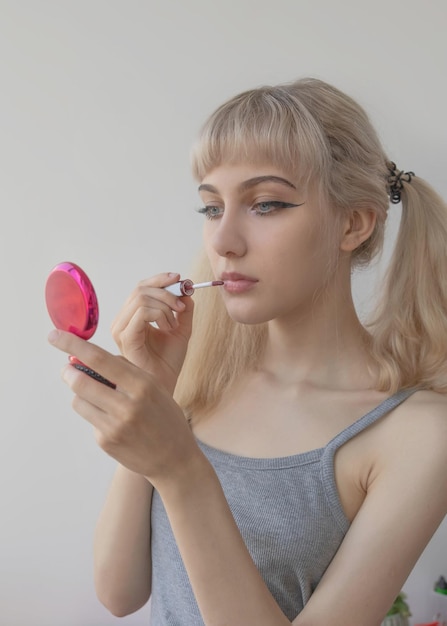 Foto la giovane donna bionda si dipinge le labbra con il trucco e si guarda in un piccolo specchio