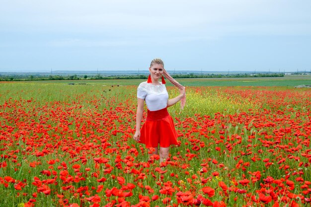 Blonde young woman in red skirt and white shirt red earrings is in the middle of a poppy field