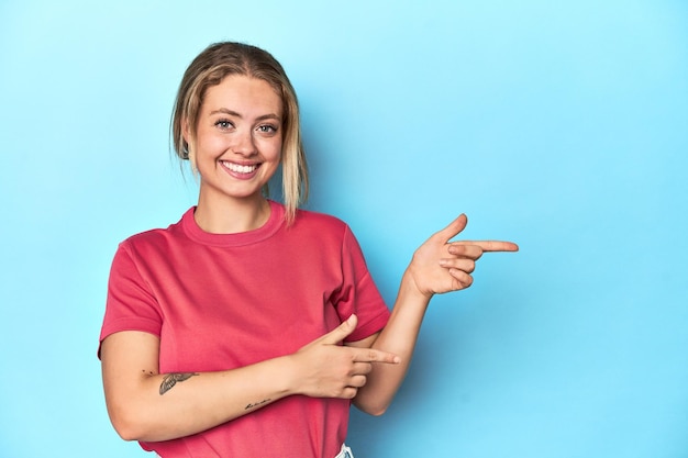 Foto giovane donna bionda in maglietta rossa su sfondo blu che punta con le dita indice