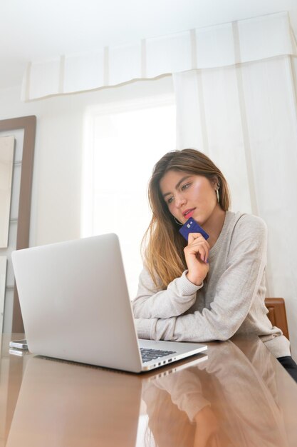 Foto giovane donna bionda pensando e guardando un prodotto su un e-commerce prima di acquistare con carta di credito