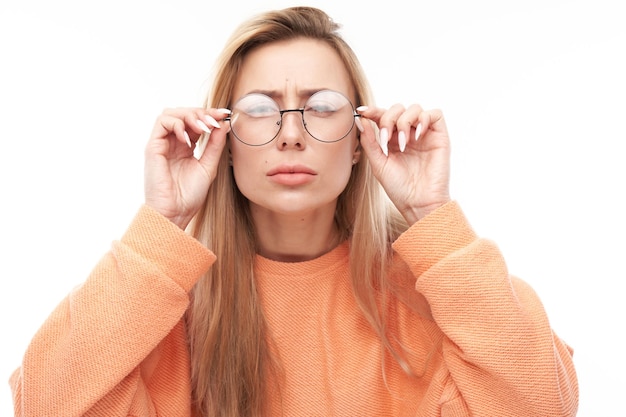 Blonde young woman wearing glasses squinting while looking at camera isolated on white background Vision problems concept