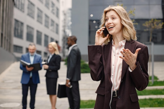 Blonde zakenvrouw staat en praat aan de telefoon voor een modern kantoor