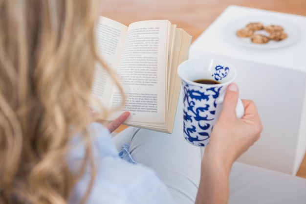 Blonde zittend op de bank lezen met een kopje koffie