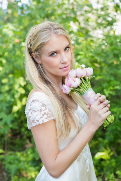 Blondebruid die camera bekijken die roze boeket houden