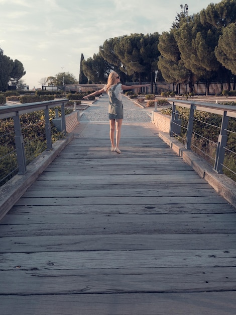 Blondehaired woman strolling relaxed on wooden bridge destressing from city life