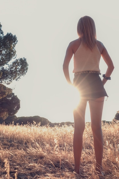 Foto donna bionda che passeggia attraverso il campo di grano in pantaloncini corti al tramonto