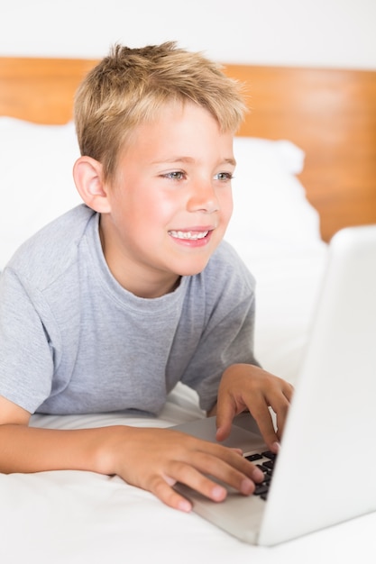 Blondejongen die op bed liggen die laptop met behulp van