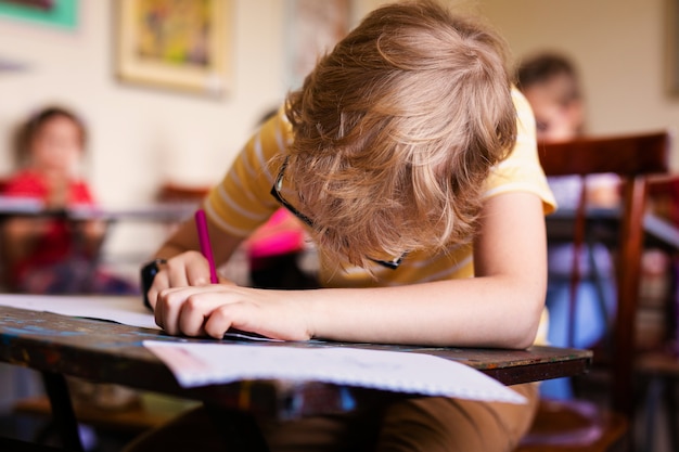 Blondejongen met glazen het trekken. Groep basisschoolleerlingen in klaslokaal op kunstklasse