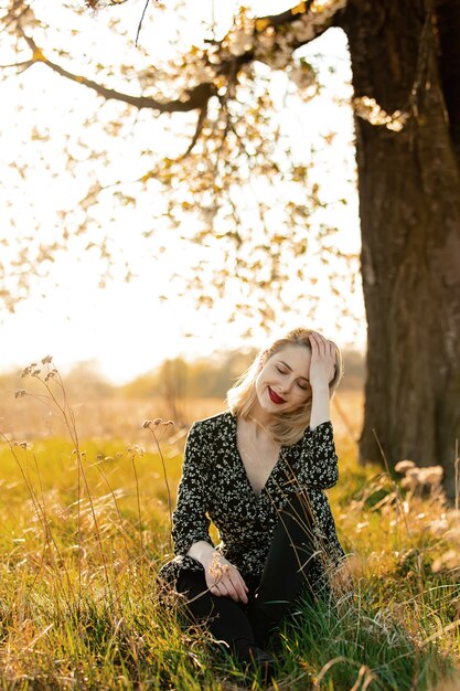 Blondemeisje dichtbij bloeiende boom bij platteland in zonsondergang