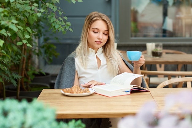 Blondemeisje het drinken koffie terwijl het lezen van een boekzitting op de zitkamer van het koffie.