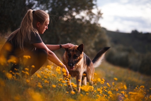 Foto blondemeisje het spelen met duitse herdershond op een gebied van gele bloemen