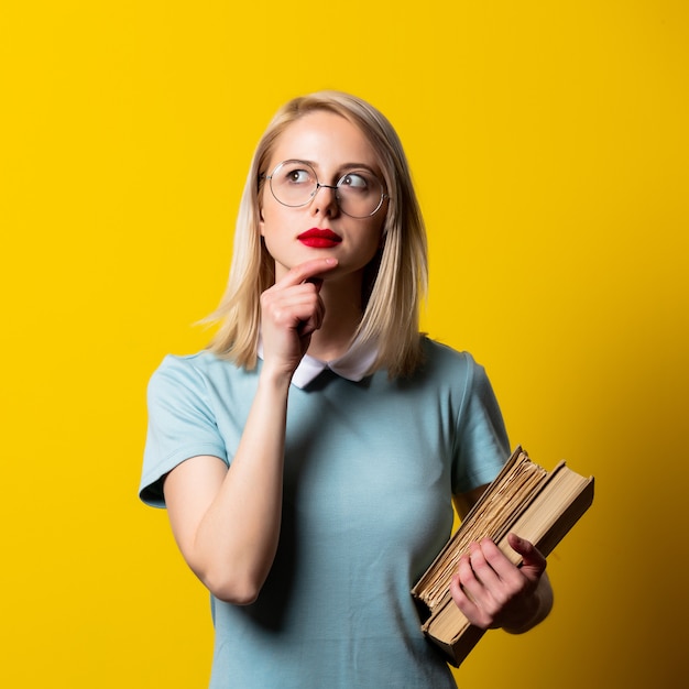 Blondemeisje in blauwe kleding en glazen met boeken op gele ruimte