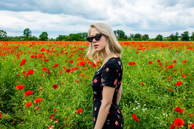 Blondemeisje in zonnebril op papaversgebied in de zomertijd