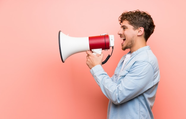 Blondemens die over roze muur door een megafoon schreeuwen