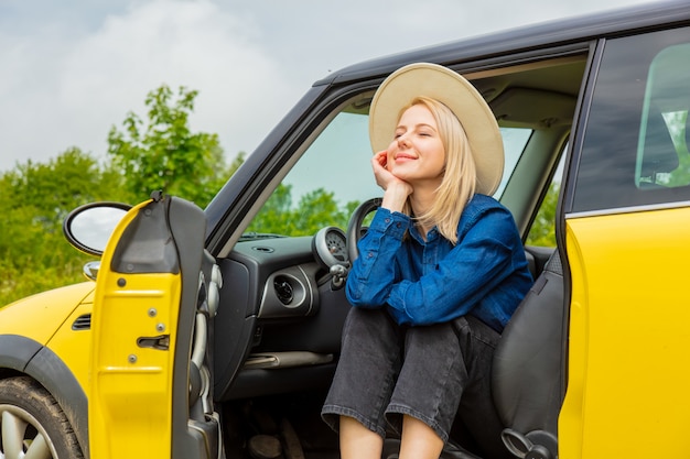 Blondeveedrijfster in hoed siiting in een auto bij platteland