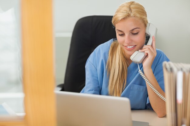 Foto blondeverpleegster die naast laptop roept