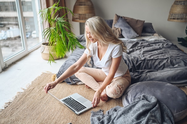 Blondevrouw die aan laptop in de slaapkamer werken